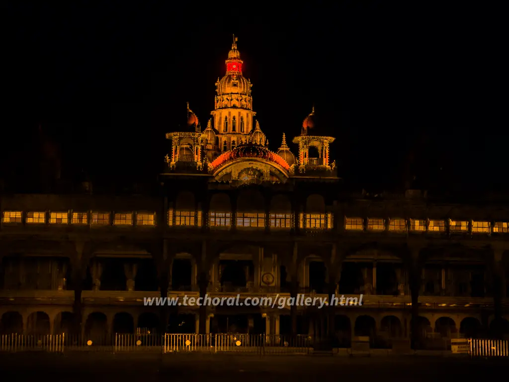 Nighttime vista of Mysore Palace adorned with vibrant lights, casting a radiant glow against the dark sky. The dazzling illumination highlights the intricate architecture and regal charm of the palace, offering a captivating sight to behold. Experience the enchanting allure of Mysore Palace at night, a spectacle that evokes awe and admiration.